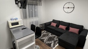 Un salon moderne avec un canapé, un téléviseur fixé au mur, un four à micro-ondes et une petite table.