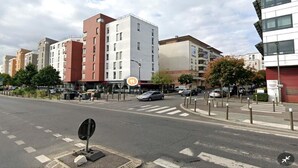 Un immeuble à plusieurs étages comprenant des espaces résidentiels et commerciaux, avec notamment un magasin dont la devanture est visible depuis la rue.