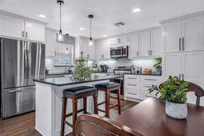 A modern kitchen with white cabinetry, stainless steel appliances, and a central island with bar stools. - The Green Emerald Close to Down Town Brenham (Brenham)