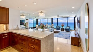 A modern kitchen with a large island, a dining area with a view, and a living room with a large window overlooking the ocean.