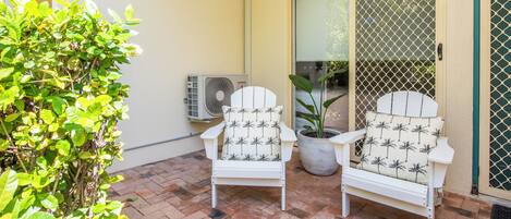 Two white chairs with palm tree patterns, a potted plant, and an air conditioning unit on a tiled patio.