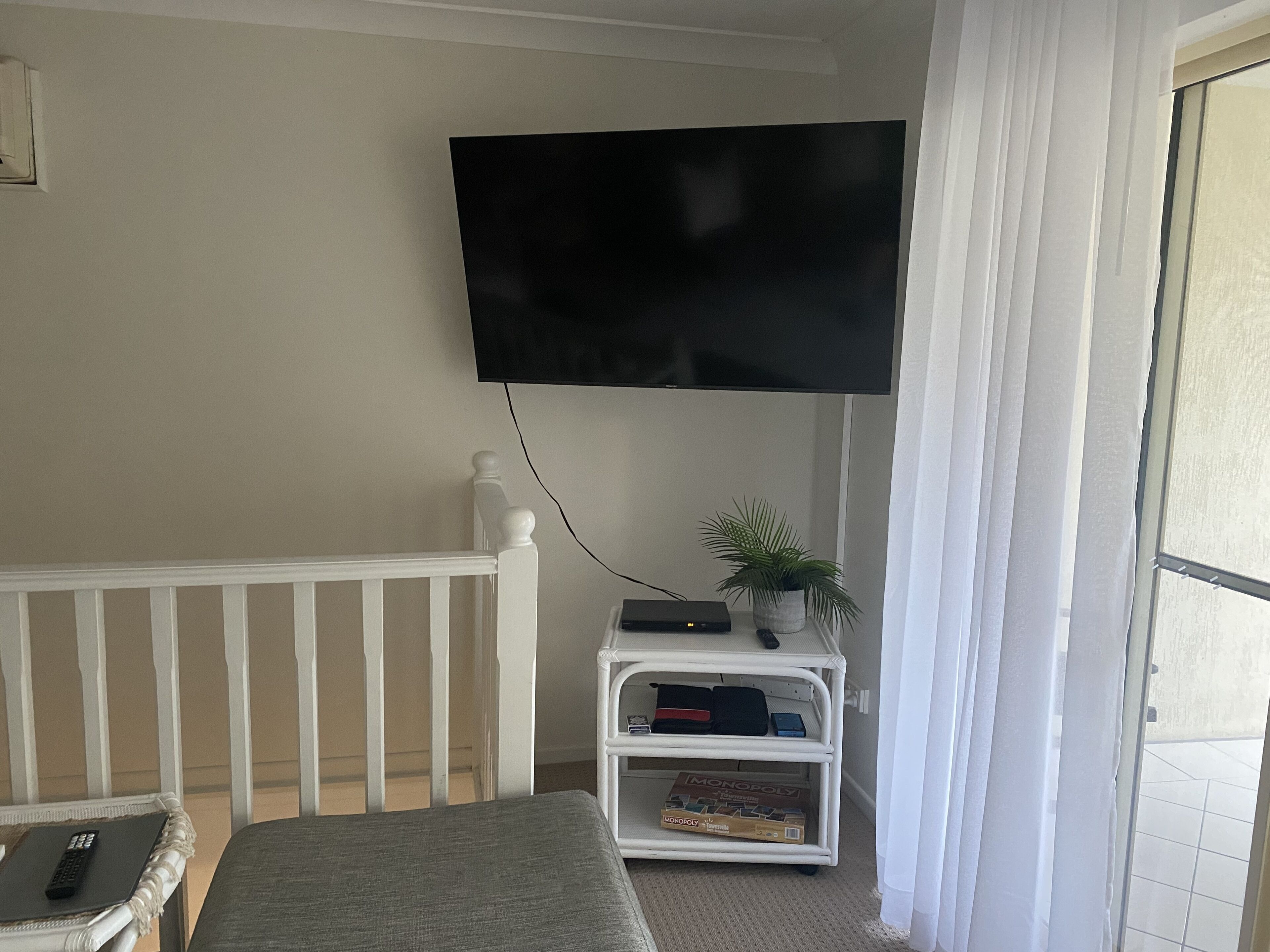 Una sala de estar con un televisor montado en la pared, un mueble blanco de entretenimiento con una planta, y un sofá gris.