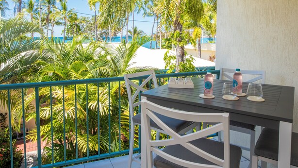 Un balcon avec une table et des chaises, donnant sur un jardin de palmiers et une piscine.