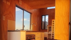 A compact kitchen with wooden walls, a window, and a built-in oven. - Eco tiny home williwa (Portland)