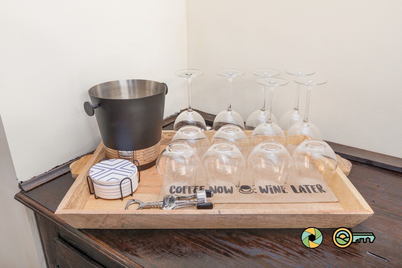 A tray with a stainless steel pot, wine glasses, and a placemat with the text "COFFEE NOW WINE LATER".