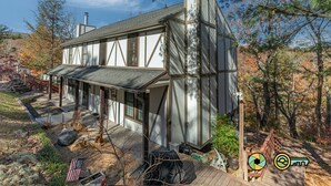 A modern house with a large deck, a chimney, and a view of the surrounding trees.