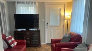Ein Wohnzimmer mit zwei roten Ledersofas, einem Holztisch, einem Flachbildfernseher auf einer Anrichte und einer Stehlampe.