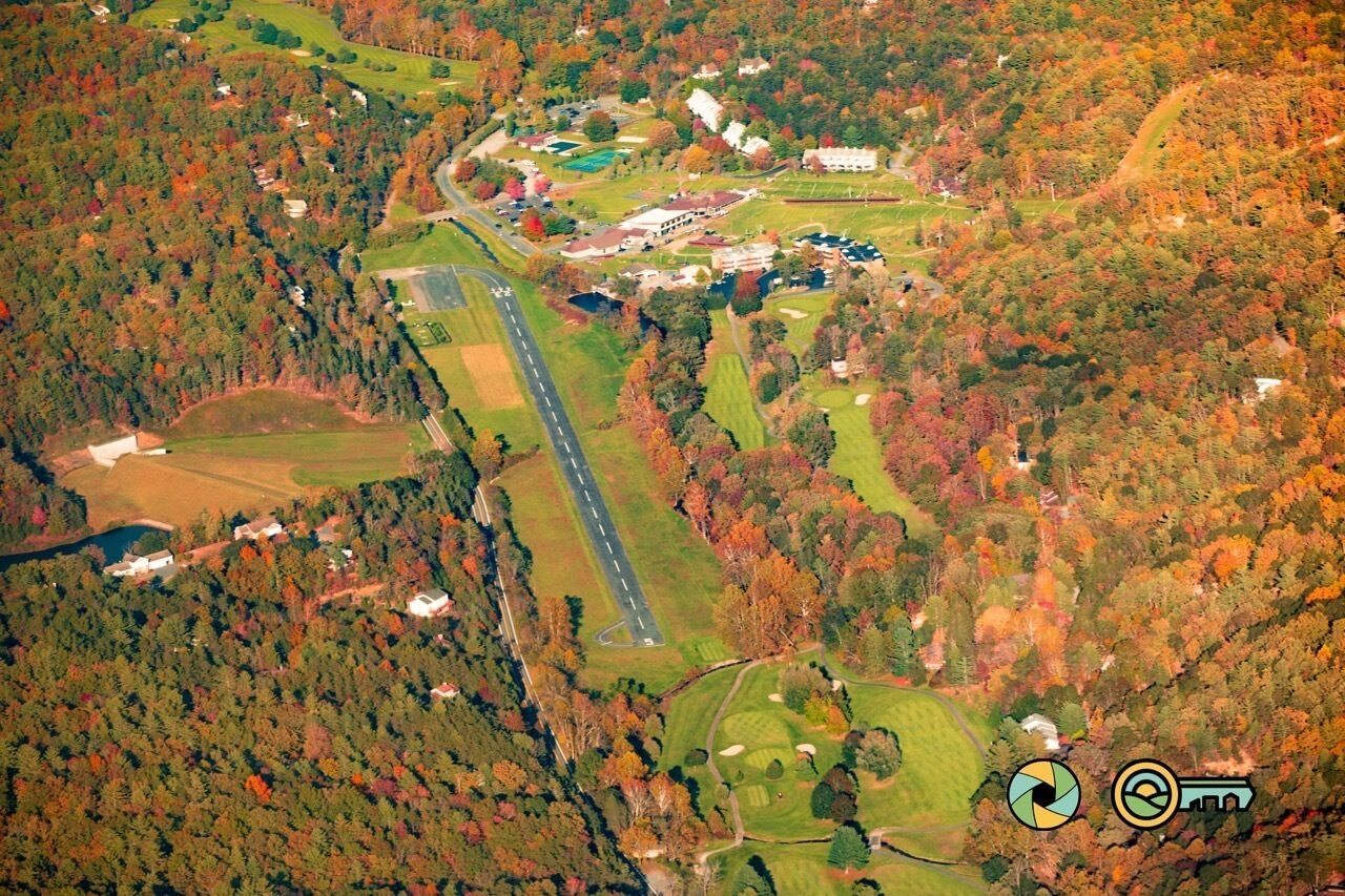 Vista aérea de un campo de golf con una pista de aterrizaje, rodeado de bosques densos y zonas residenciales.