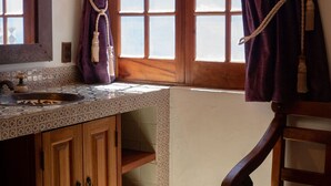 A bathroom with a wooden vanity, a mirror, a window with curtains, and a hanging towel.