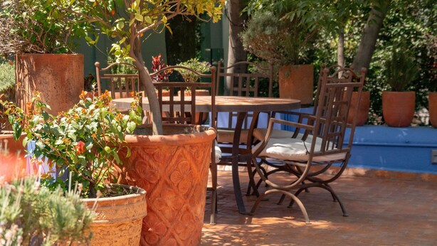 An outdoor patio with a wooden table and chairs, surrounded by terracotta pots and potted plants.