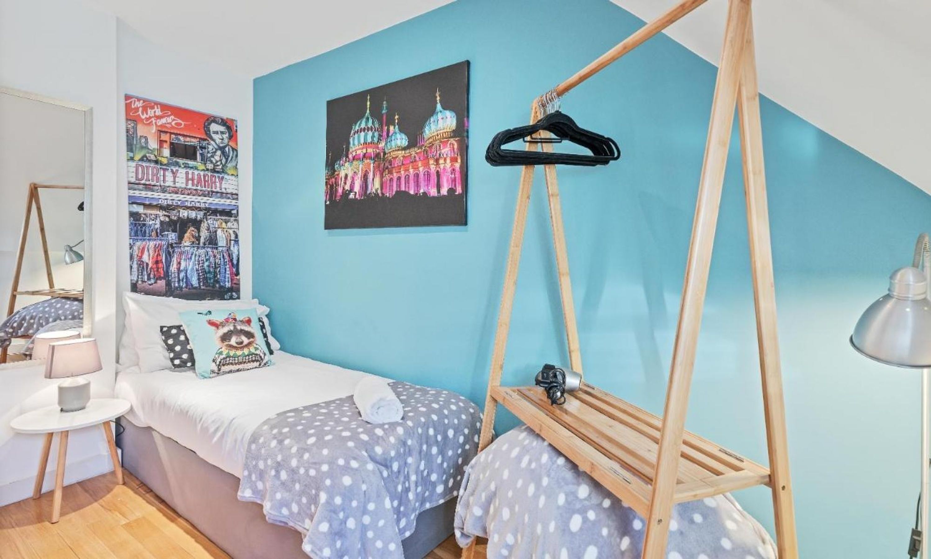 A bedroom with a bed, a hanging clothes rack, a lamp, and two posters on the wall.