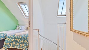 A bedroom with a sloped ceiling, a skylight, a bed with patterned bedding, a white radiator, and a staircase. - Majestic Mews Apartment Super Central Sleeps 2 to 8 Guests Free Wifi (Brighton)