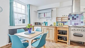 A compact kitchen with a dining area, featuring a microwave, toaster, kettle, and stove. - Pebble Mews House - Sleeps 6 to 8 Guests (Brighton)