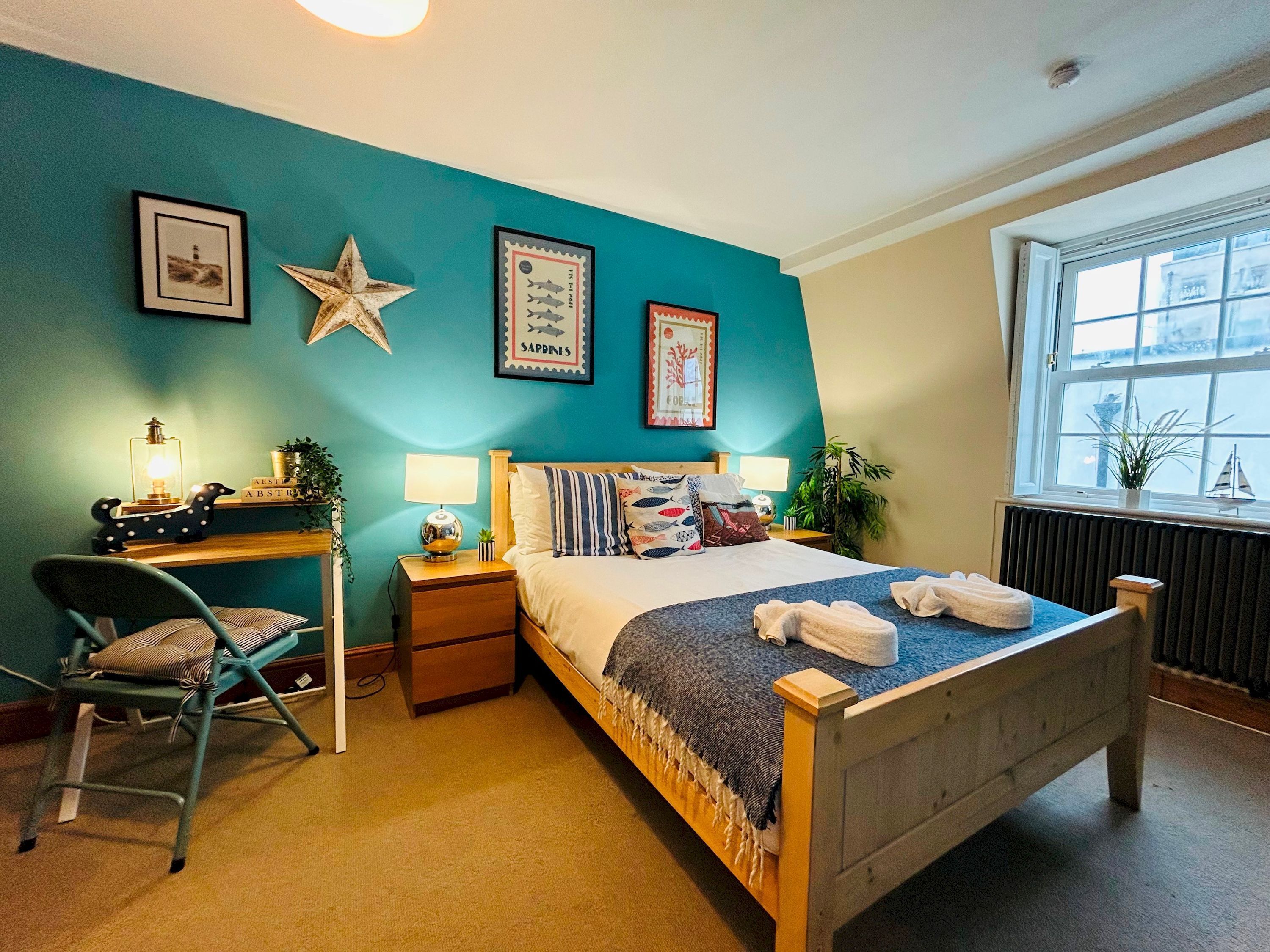 A bedroom with a bed, bedside tables, a desk, a chair, and a window.