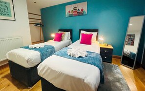 A hotel room with two beds, a nightstand with a lamp, and a wall-mounted artwork.