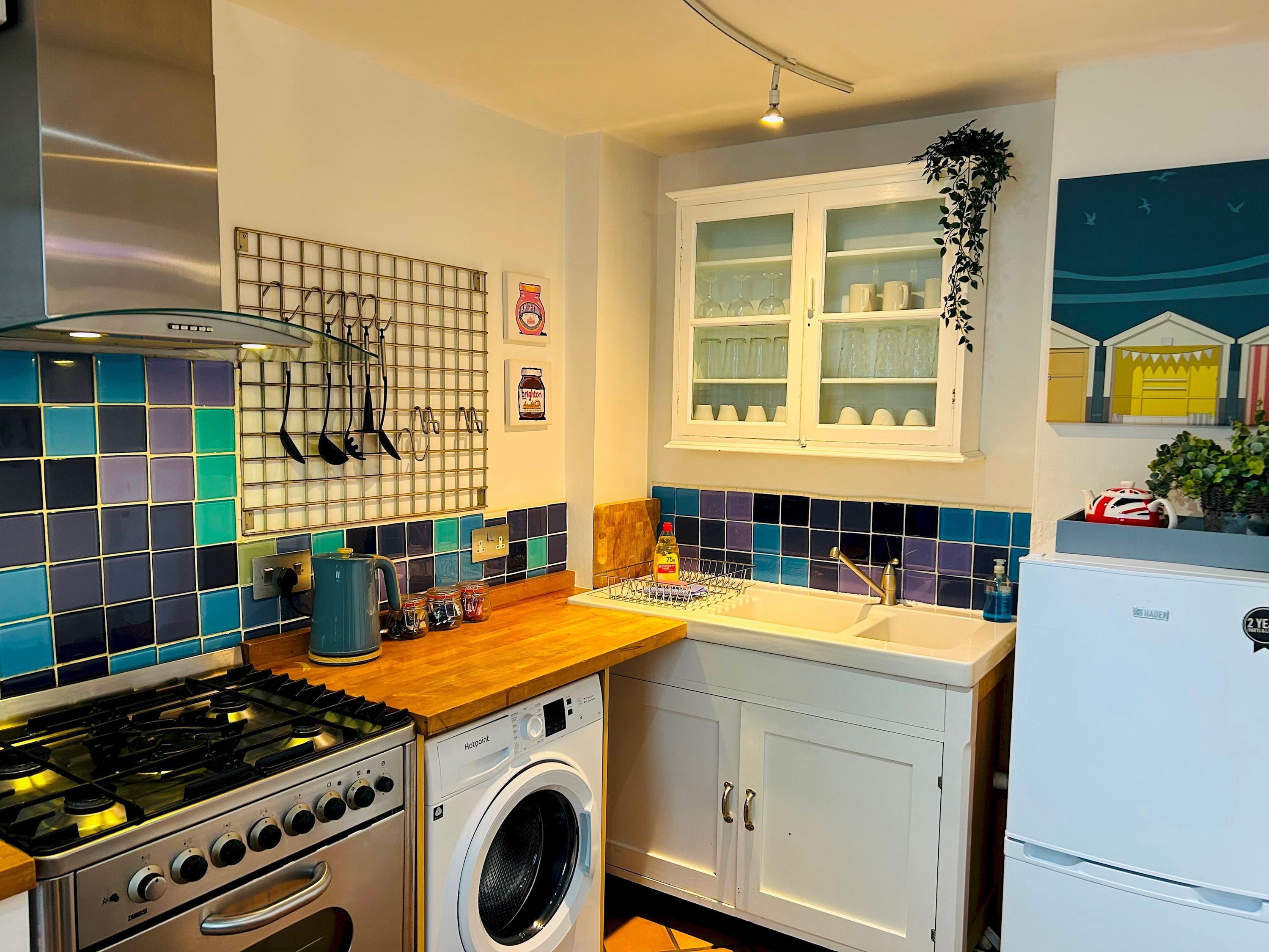 A compact kitchen with a gas stove, a washing machine, a sink, and a cabinet with glass doors.