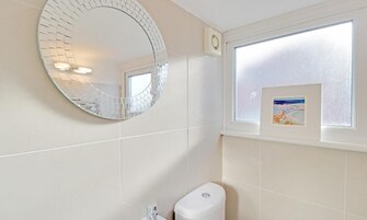 Un baño con inodoro, un espejo redondo y una ventana con marco de fotos.