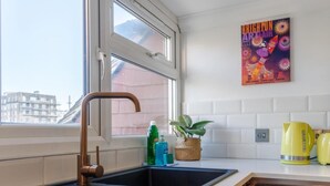 A modern kitchen with a large window, a stainless steel sink, and a yellow kettle on the counter.