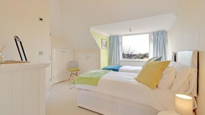 A bedroom with two beds, a window with curtains, a chair, and a lamp.