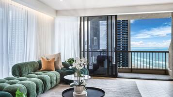 Ein modernes Wohnzimmer mit einem grünen Sofa, einem runden Couchtisch mit Pflanze und Blick auf den Ozean durch große Fenster.
