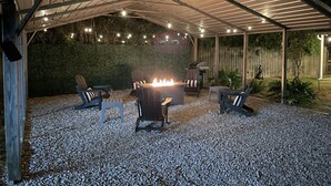 Un espace extérieur couvert, aménagé en patio, avec un foyer, des sièges et des guirlandes lumineuses.