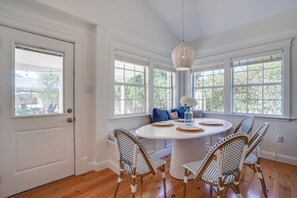 A dining area with a round table, wicker chairs, and a hanging light fixture. - On Main St! Private Heated pool, Golf cart included, Sleeps 10 (Bay St. Louis)