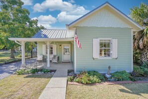 A light green house with a porch, a small garden, and an American flag. - On Main St! Private Heated pool, Golf cart included, Sleeps 10 (Bay St. Louis)