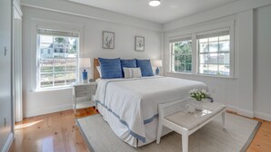 Une chambre à coucher avec un grand lit, deux fenêtres, un ventilateur de plafond et une table de chevet avec une lampe.