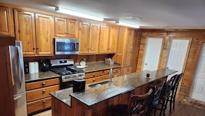 A kitchen with wooden cabinets, a stainless steel refrigerator, a microwave, a stove, and a granite countertop. - NEWLY RENOVATED Houseboat Located in Venice Marina (B Dock) (Venice)