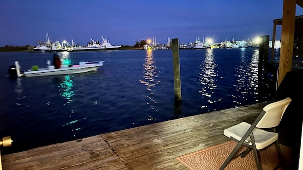 A wooden deck with a chair and a fishing rod, overlooking a marina at night with boats and lights. - NEWLY RENOVATED Houseboat Located in Venice Marina (B Dock) (Venice)