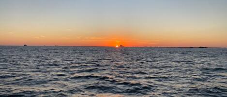 Un atardecer sobre un mar tranquilo con tierra a lo lejos en el horizonte.