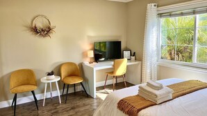 A hotel room with a bed, two chairs, a desk with a TV, a small table, and a window with a view of greenery. - Cozy, spacious 4B4B house with high-speed internet near Disney (West Covina)