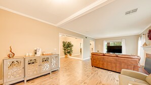 A spacious living room with a wooden floor, a brown leather sofa, a white cabinet with decorative patterns, and a flat-screen TV. - Cozy, spacious 4B4B house with high-speed internet near Disney (West Covina)