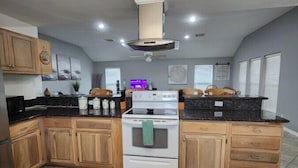 A kitchen with wooden cabinets, a white stove, and a black countertop. - Bounty Pet Friendly · Entertain & Relax at our Beach Home - Pet Friendly (Galveston)