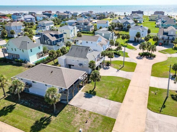 Vista aérea de una zona residencial costera con casas, palmeras y una vista despejada del océano.