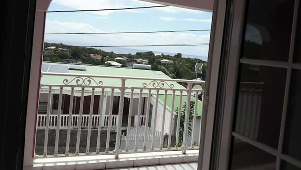 A balcony with a view of a green building and a distant landscape. - Le Gosier Spacious loft with small sea view (Le Gosier)