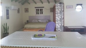 A small, cozy room with a bed, a window, a chair, and a table with a placemat. - Le Gosier Spacious loft with small sea view (Le Gosier)