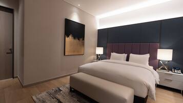 A modern hotel room with a large bed, bedside lamps, a painting on the wall, and a wooden floor.