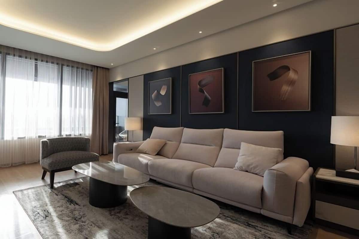 A modern living room with a beige sofa, two round coffee tables, and a large window with sheer curtains.