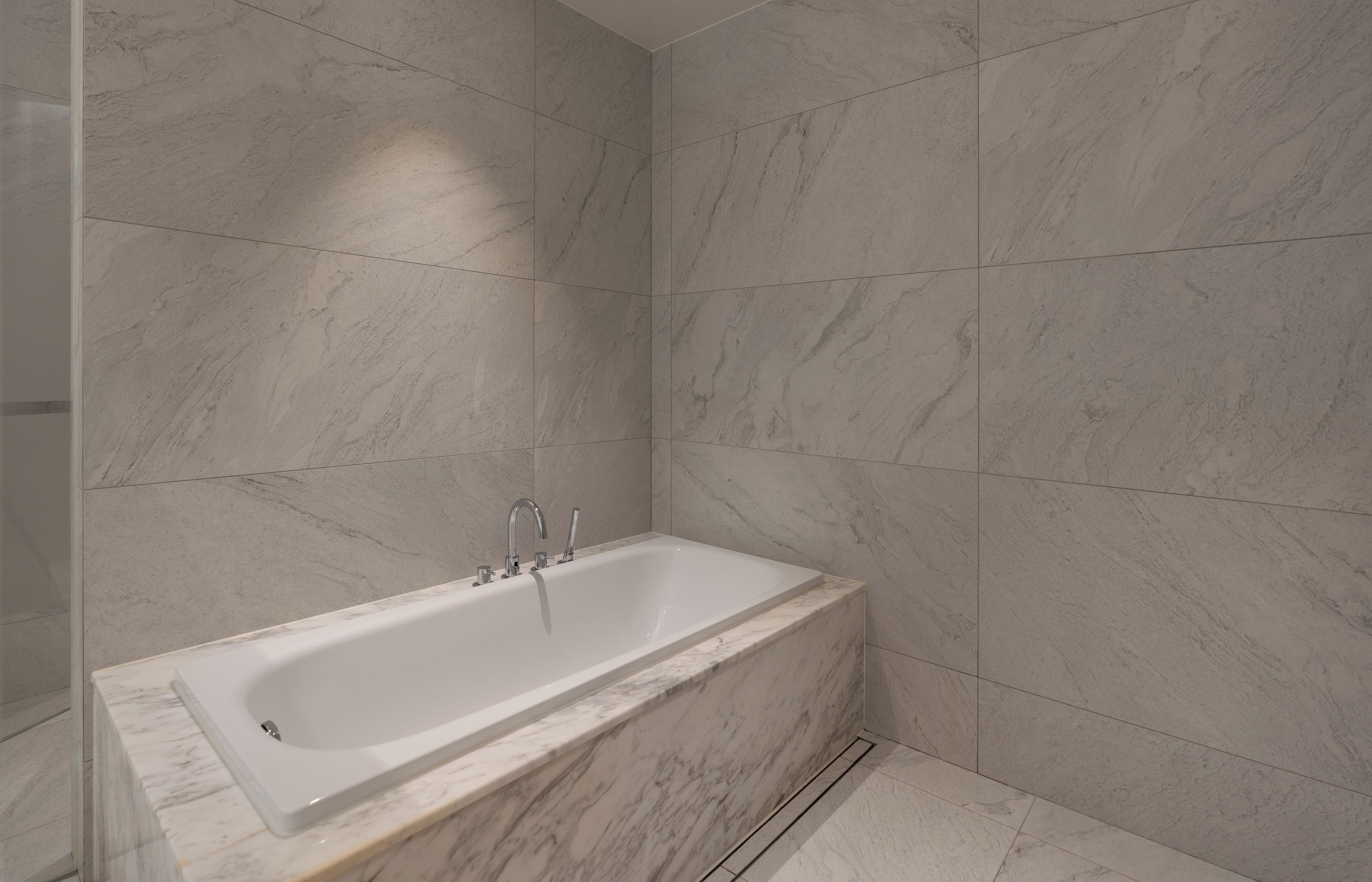 A modern bathroom with a freestanding bathtub, marble walls, and a tiled floor.