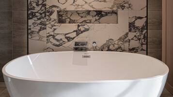 A modern bathroom with a freestanding bathtub, marble wall tiles, and a chandelier.