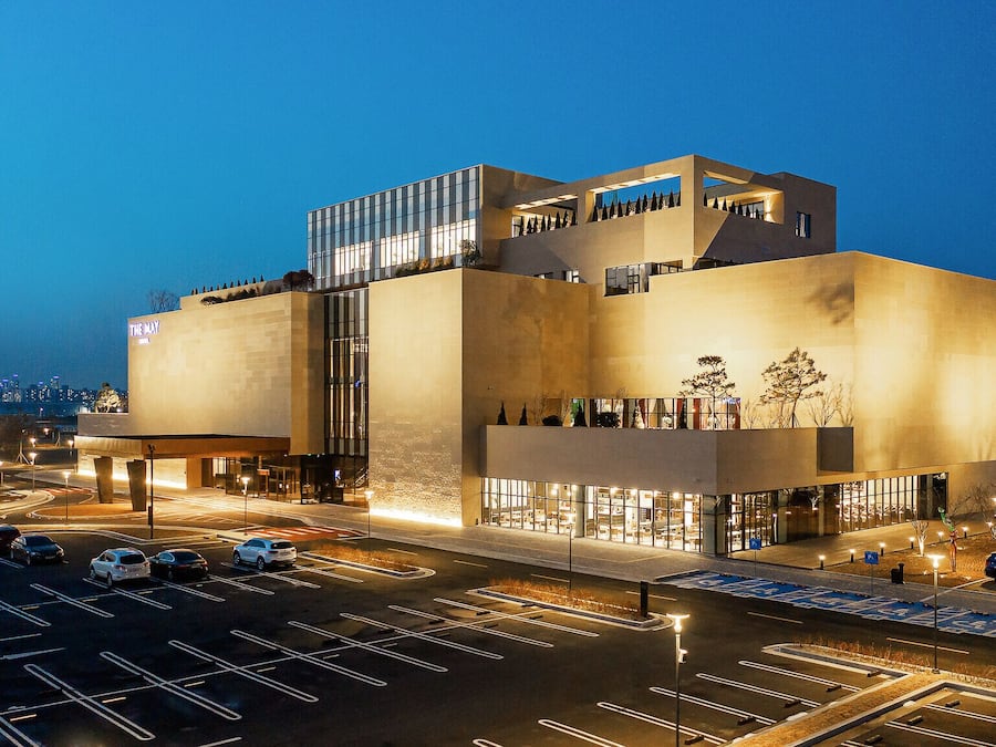A modern building with a flat roof, large windows, and a parking lot in front.