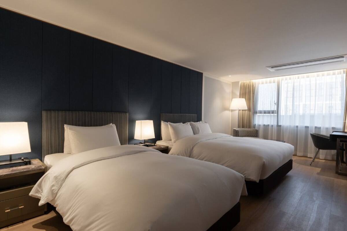 A hotel room with two beds, a desk, and a chair.