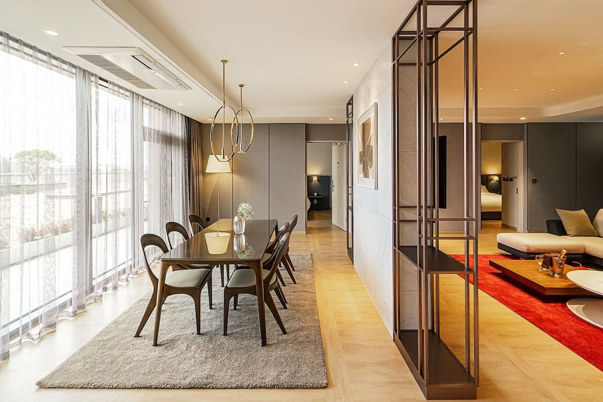 A modern living room with a sofa, a dining area with a table and chairs, and a large window with curtains.