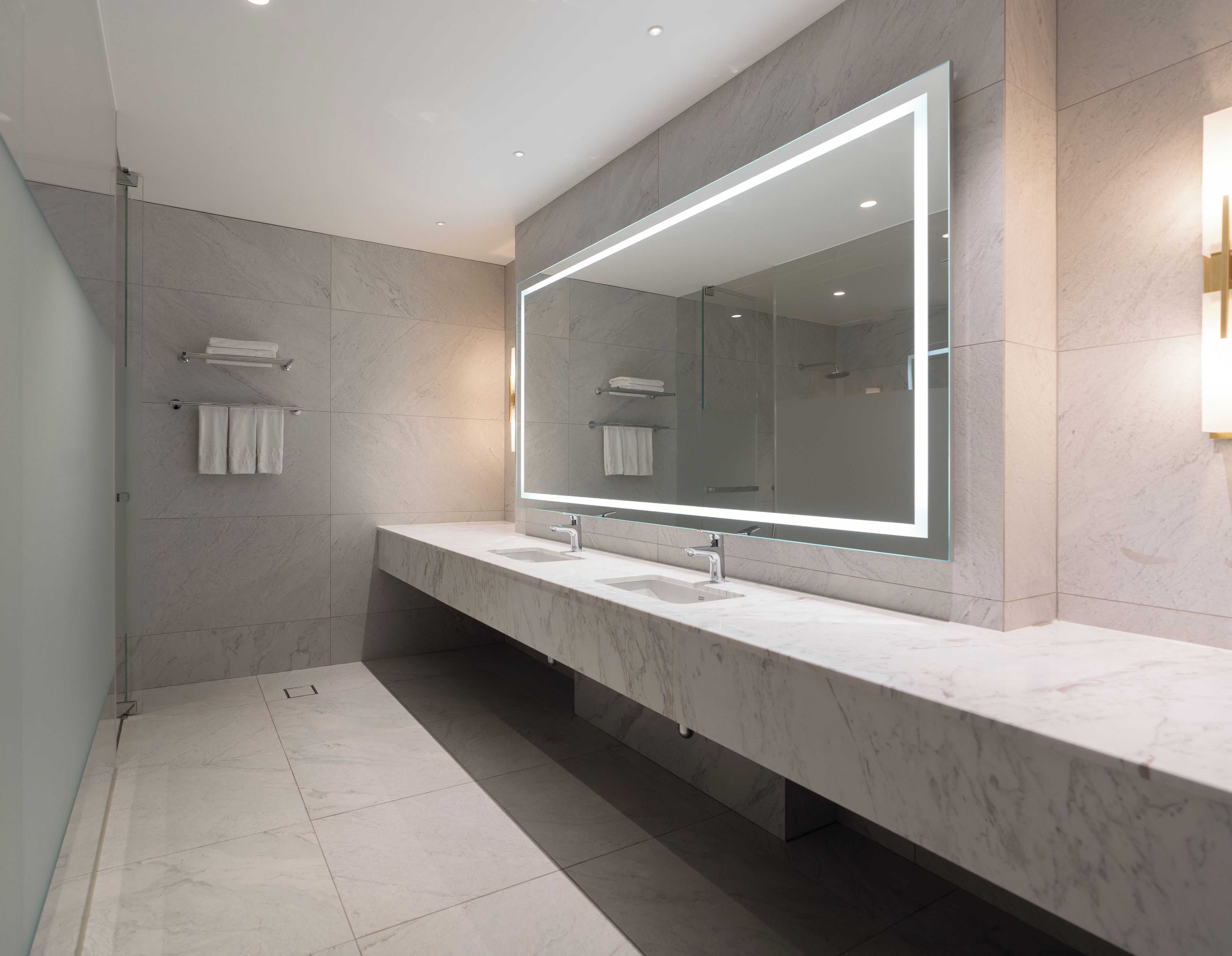 A modern bathroom with a large mirror, two sinks, and a glass shower enclosure.