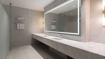 A modern bathroom with a large mirror, two sinks, and a glass shower enclosure.