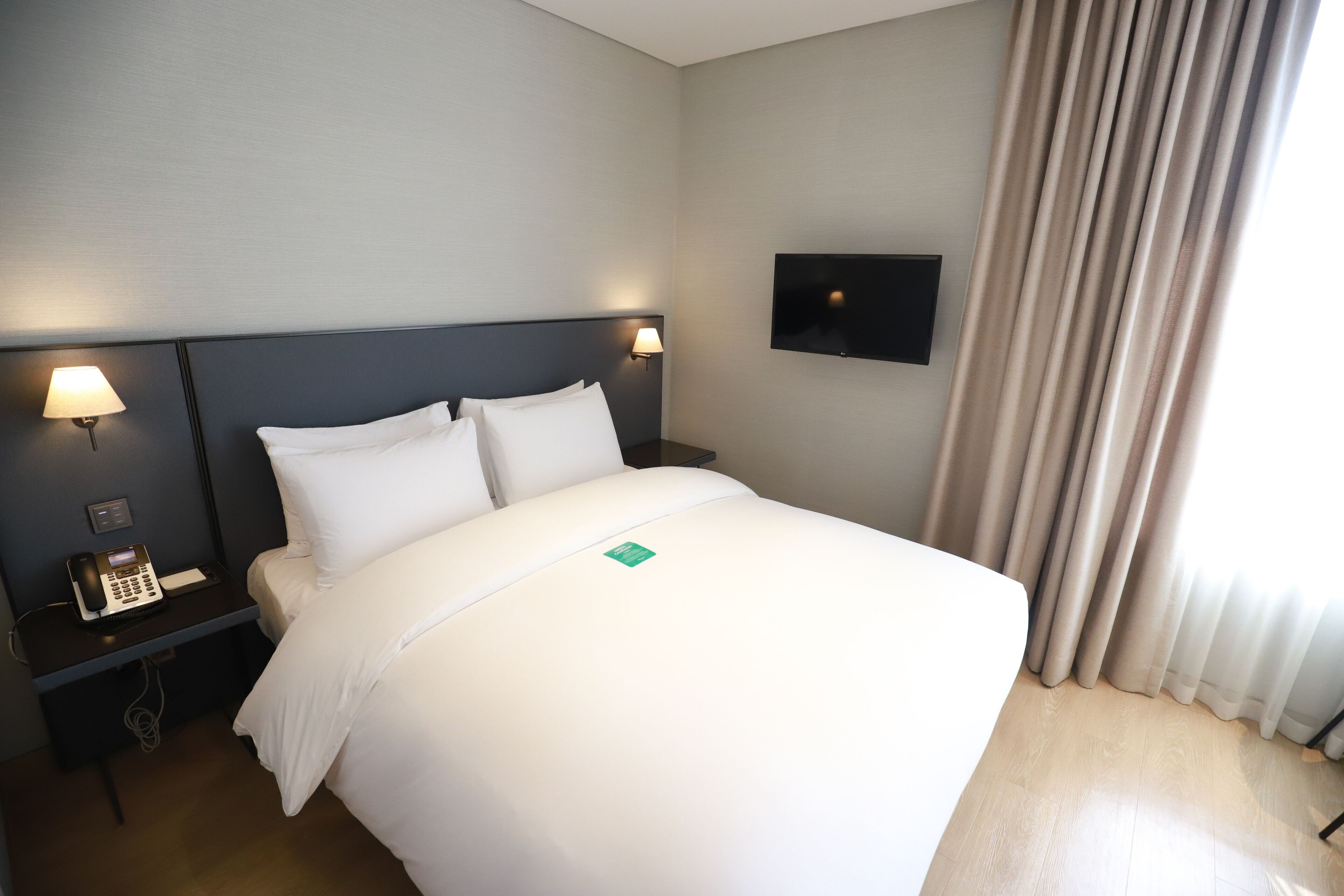 A hotel room with a bed, nightstands, a phone, a TV, and curtains.