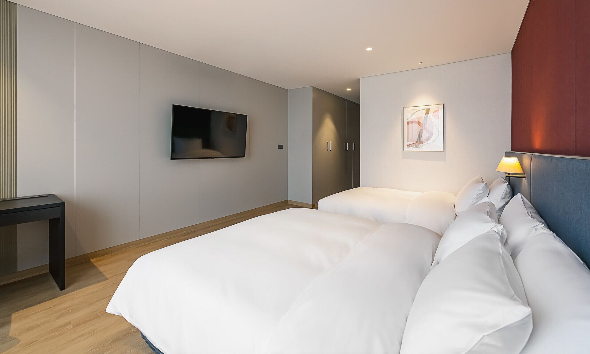 Una habitación de hotel moderna con una cama grande, un televisor montado en la pared y una mesita de noche con lámpara.