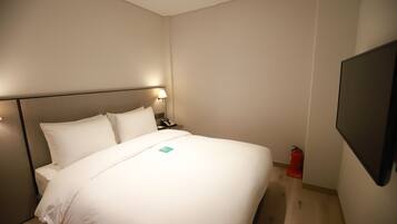 A hotel room with a bed, bedside table, lamp, and a mounted TV.