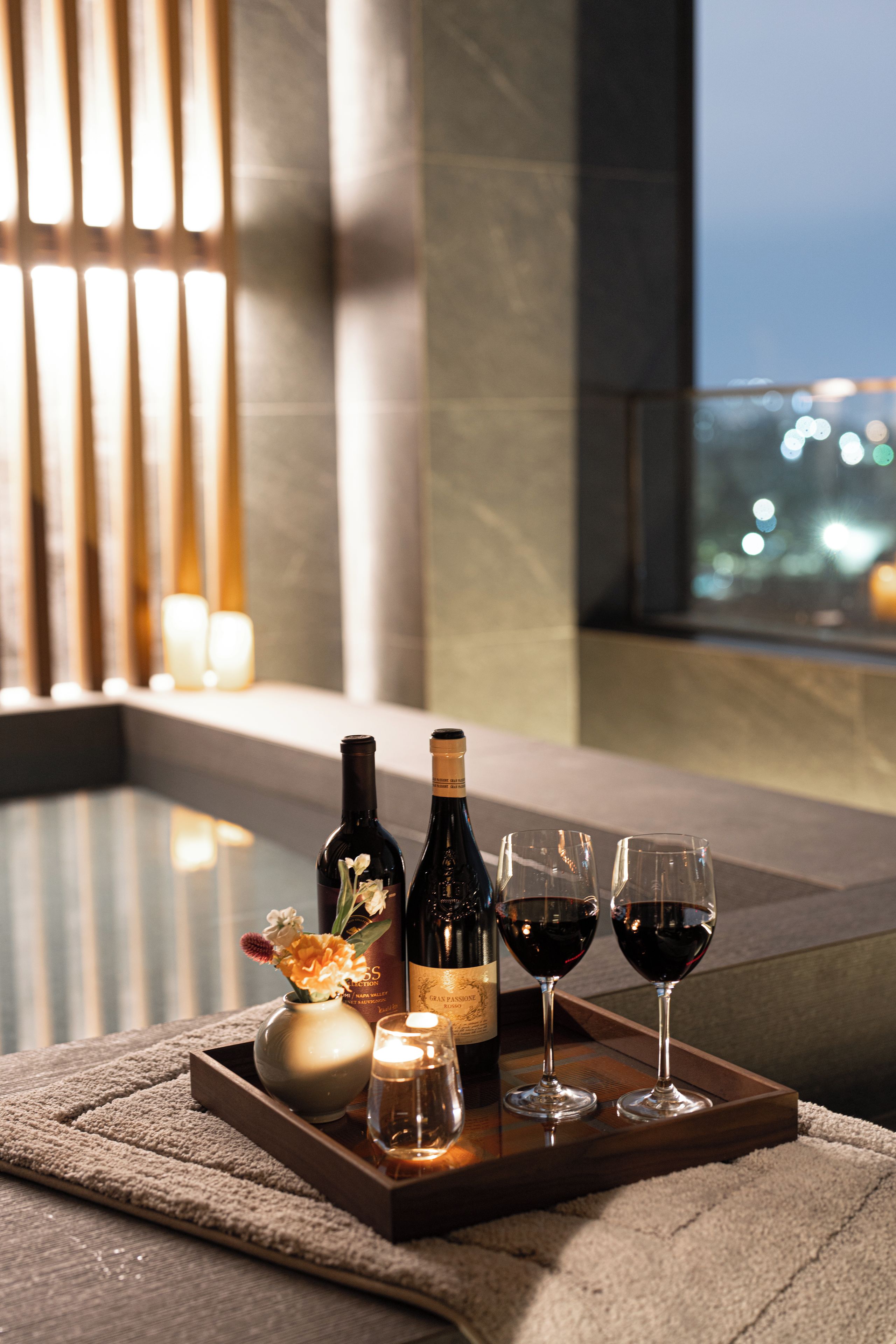 A tray with wine bottles and glasses on a table in a room with a view.